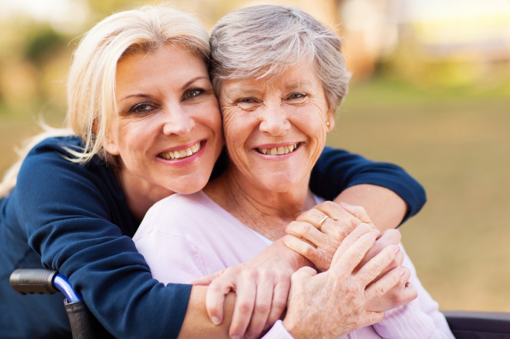 cheerful middle aged woman embracing disabled senior mother outdoors