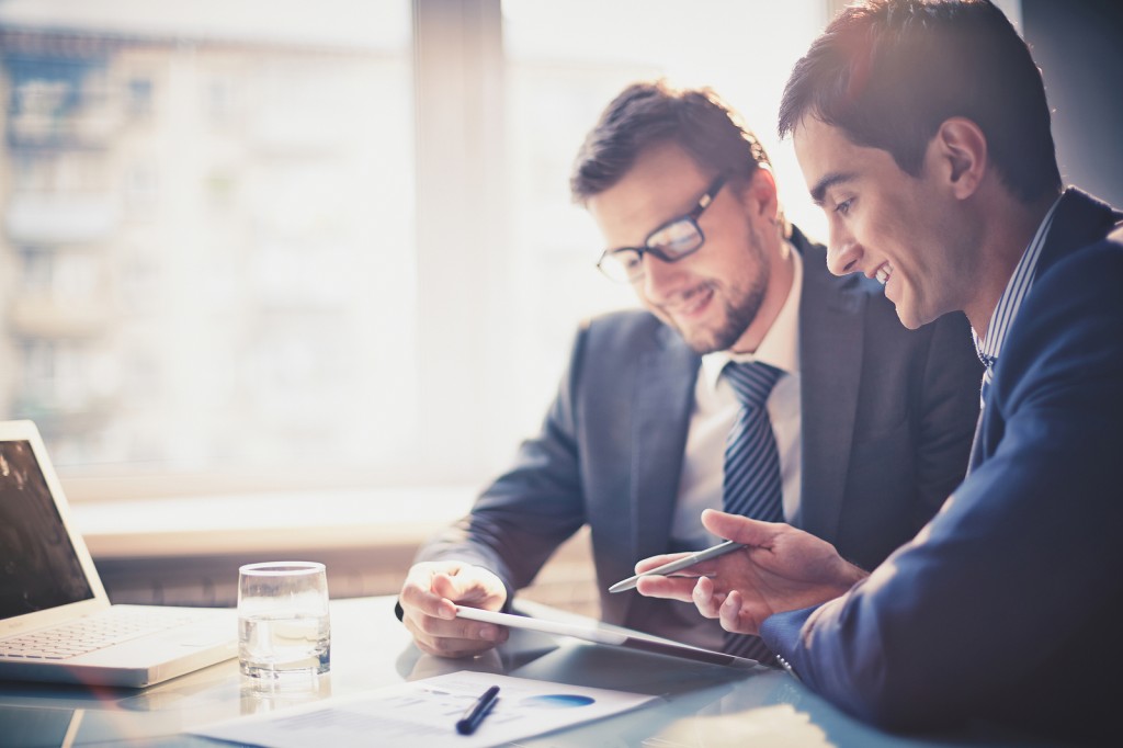 Image of two young businessmen using touchpad at meeting